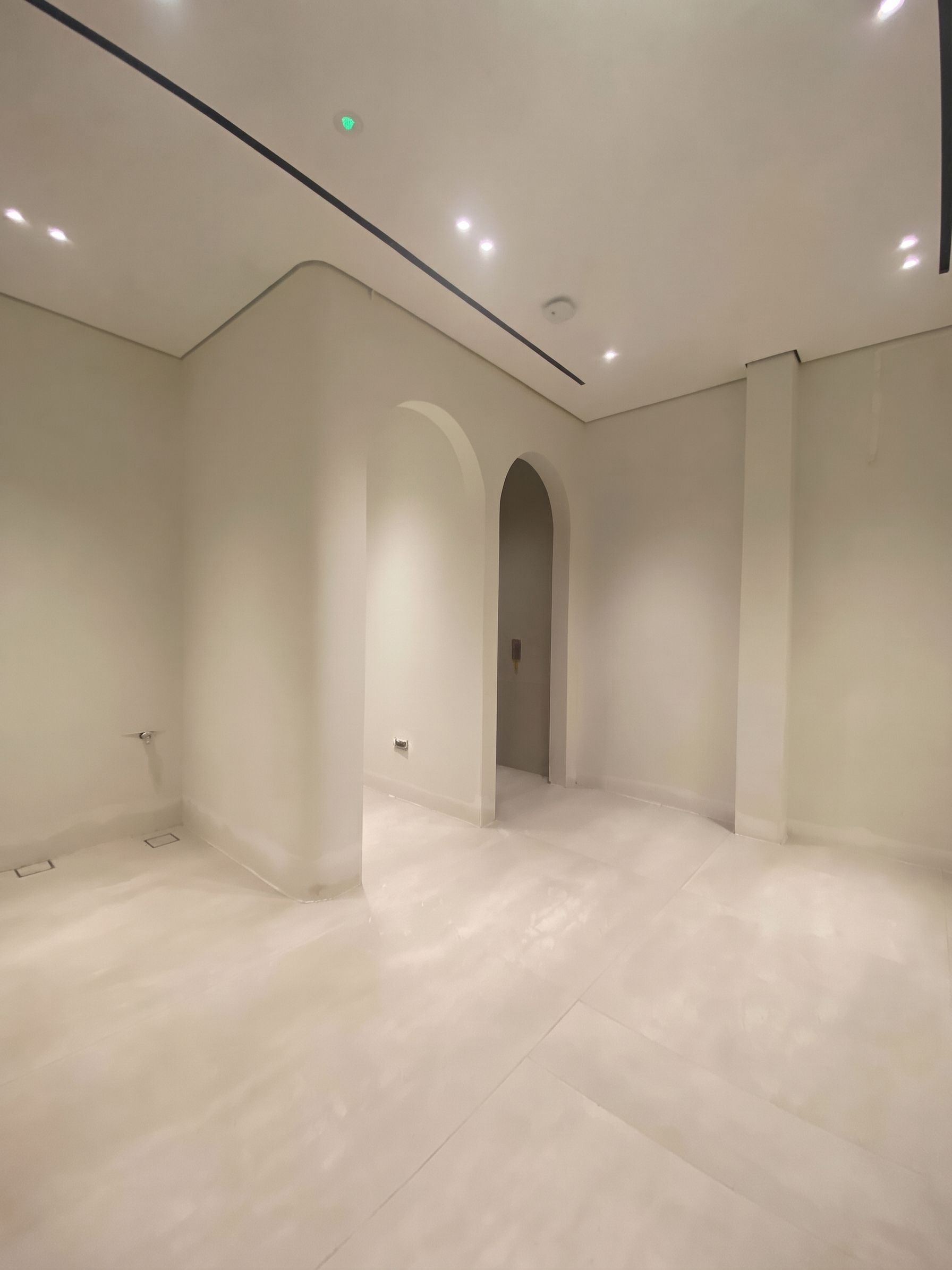 Twin plastered arches in a finished shell, under a black ceiling reveal and recessed spots, with large-format floor tiling laid.