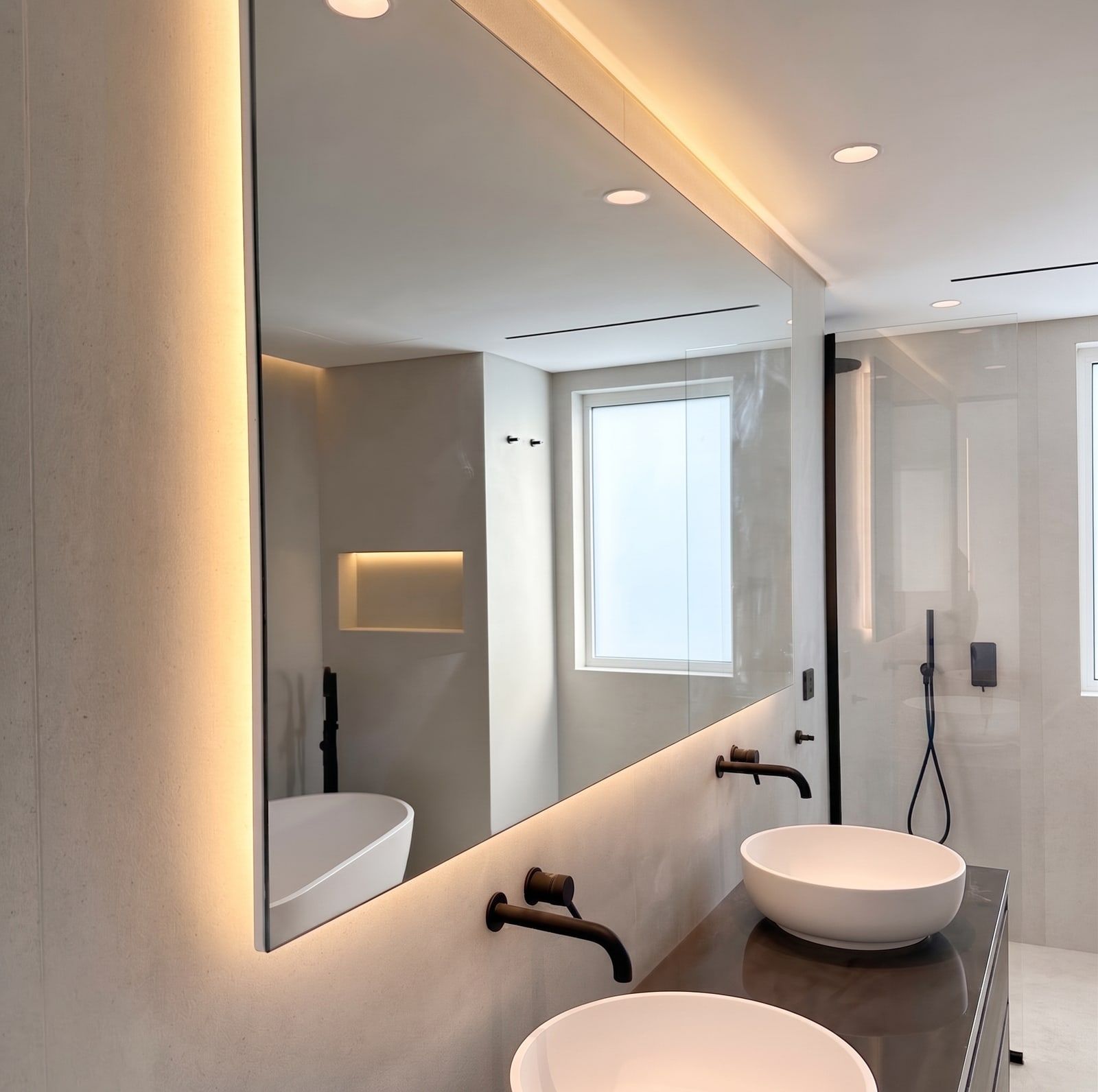 A full-width mirror floated off the wall on a warm LED reveal, over twin stone basins and wall-mounted brassware.