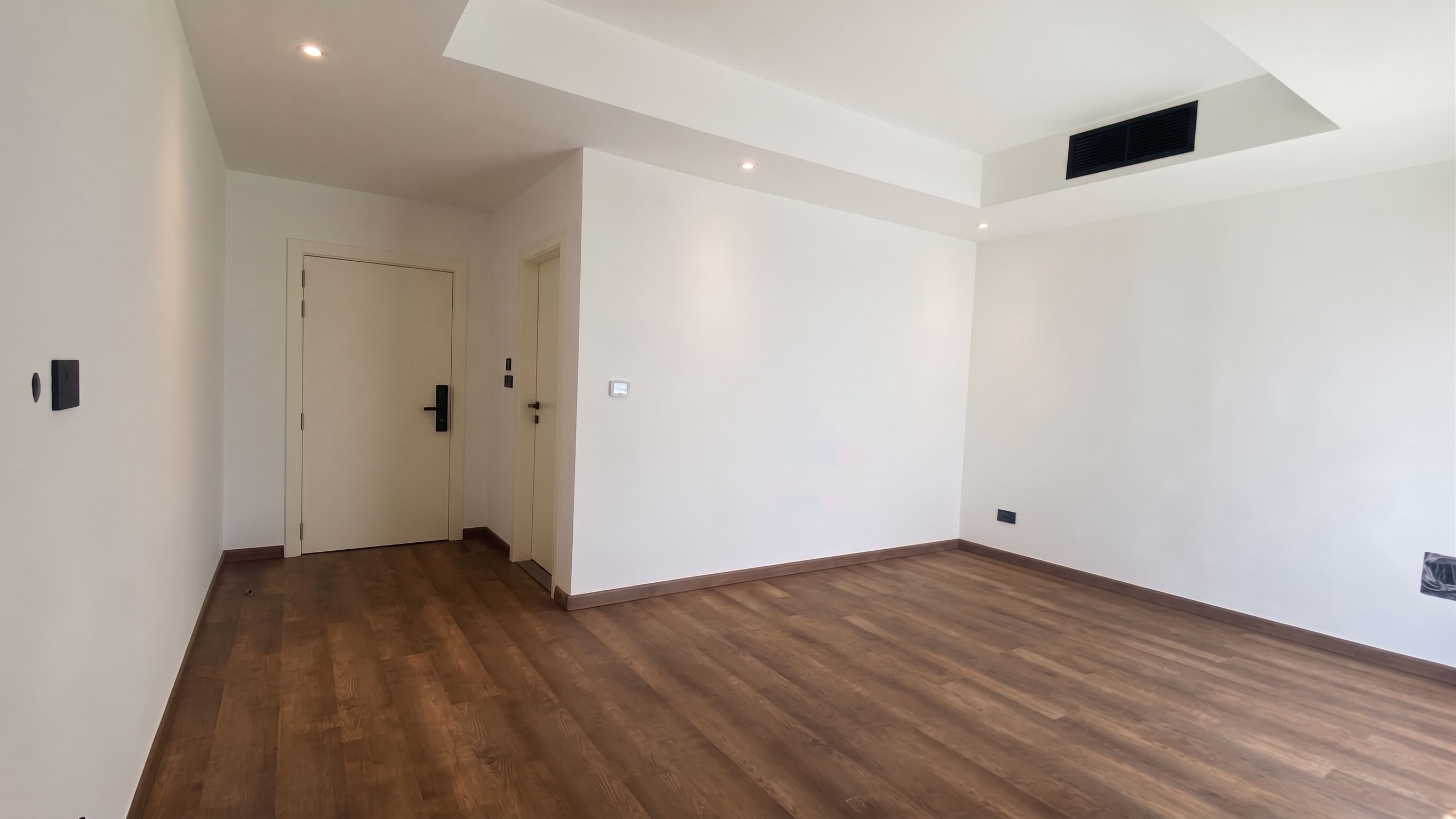 A finished bedroom waiting on furniture — oak flooring, a coffered ceiling with a lit cove, and door linings run flush to the skirting.