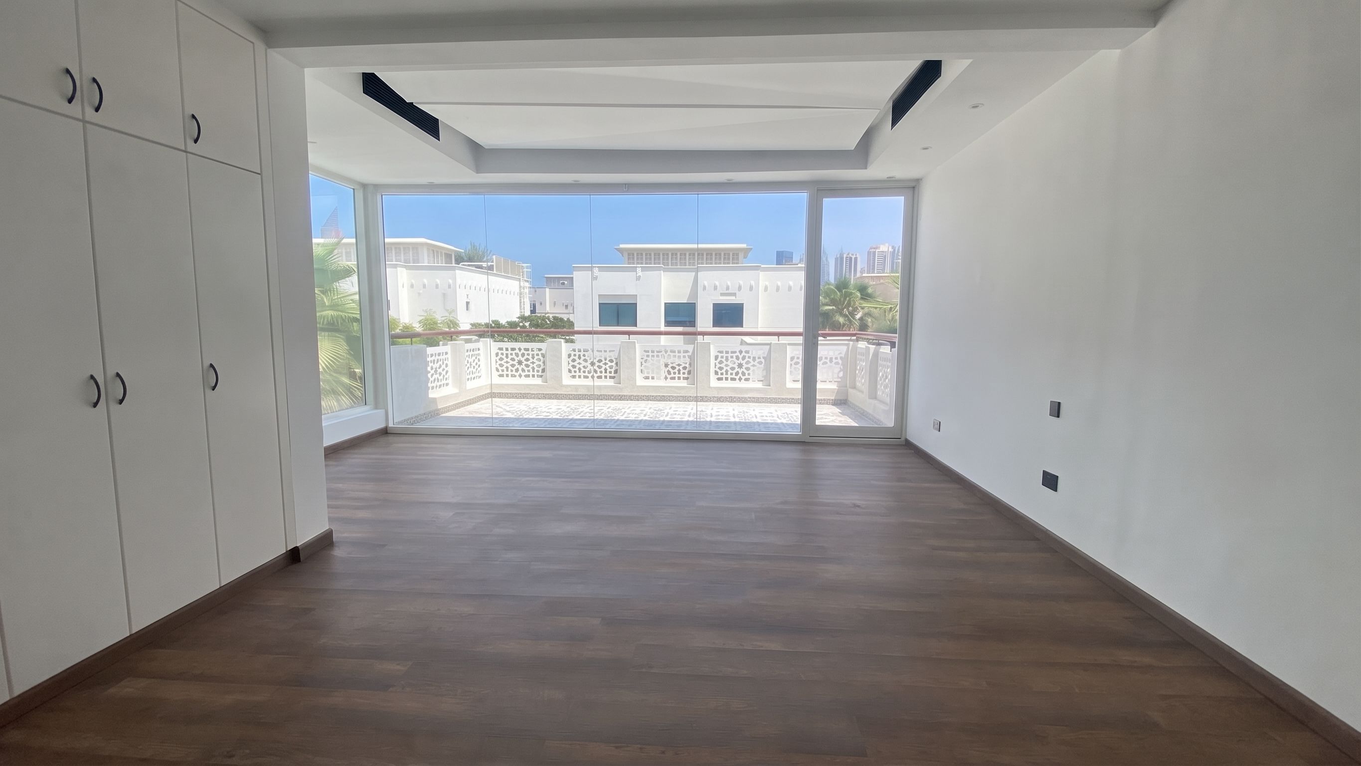 A full wall of fitted wardrobes facing sliding glazing onto a mashrabiya-screened balcony.
