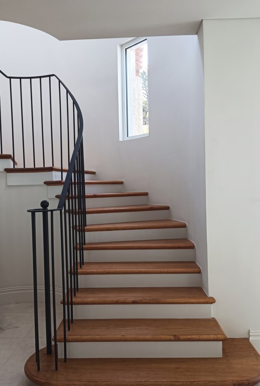 A winding flight in oak with white risers, lit by a slot window cut into the stairwell.