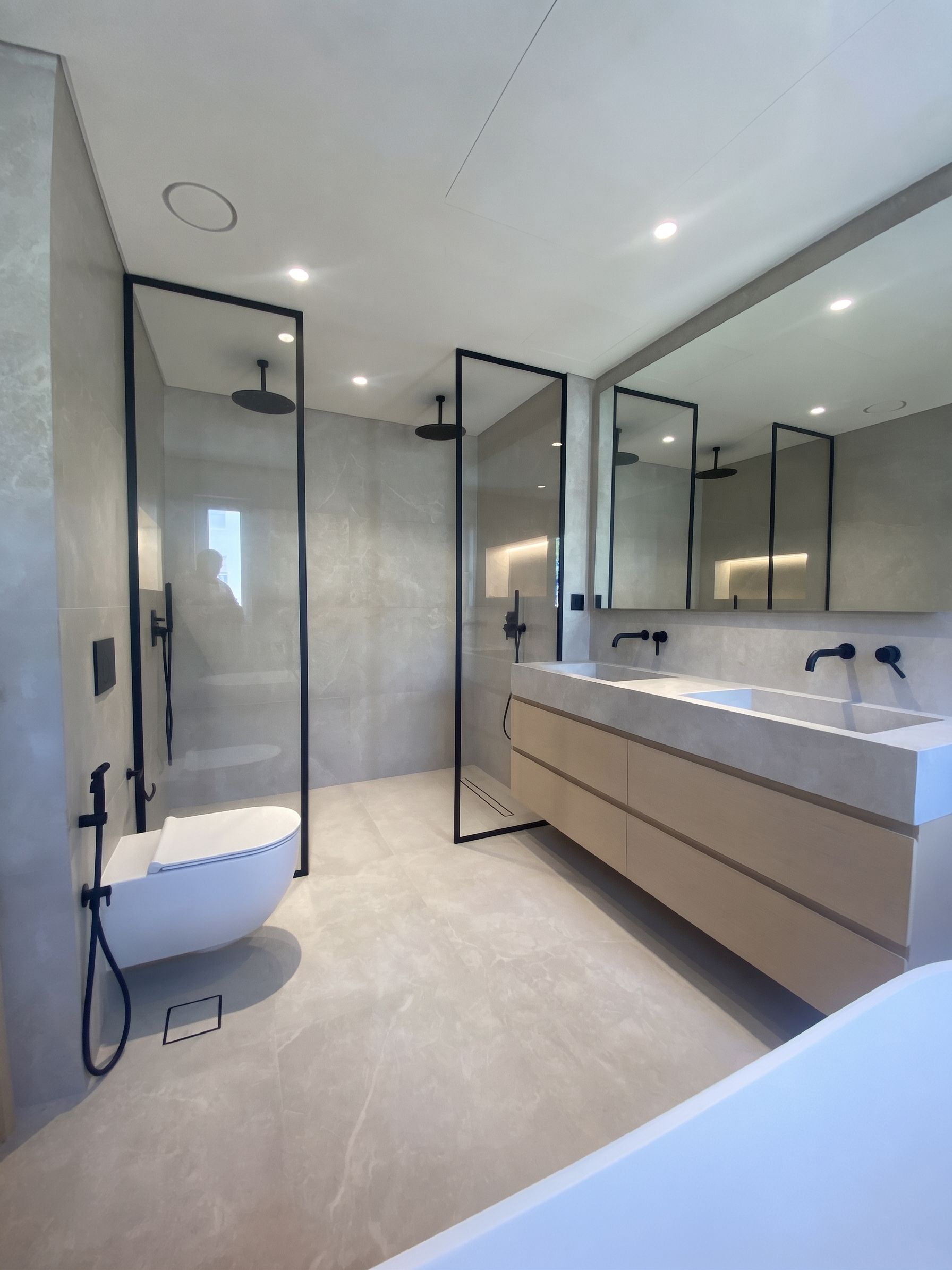 Black-framed shower screens and matt black brassware, with twin stone basins on an oak vanity and the tub set to one side.