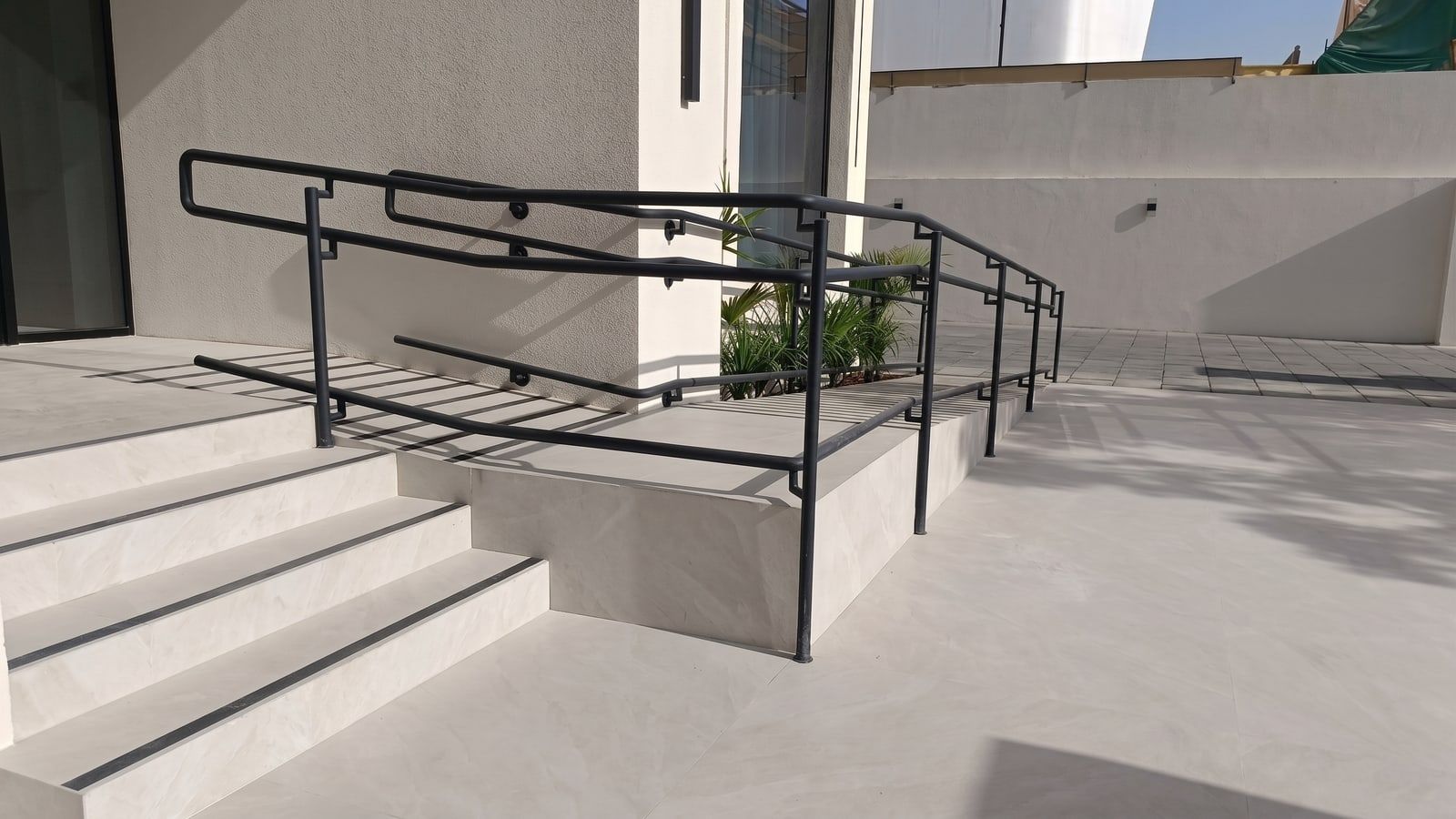 Powder-coated steel handrails and an accessible ramp in large-format porcelain paving.