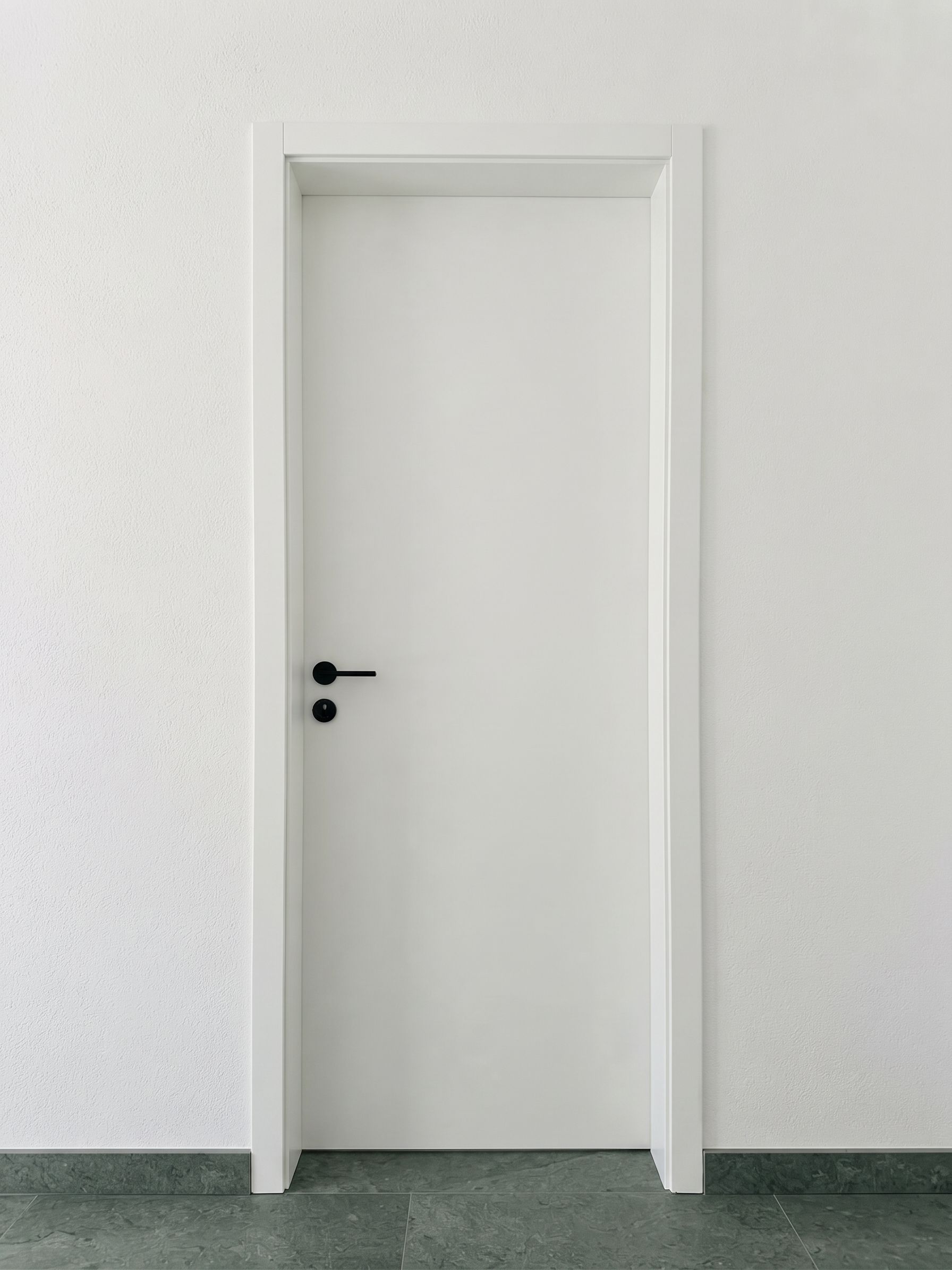 A flush door hung in a concealed frame with a shadow line in place of architrave, on a matt black lever.