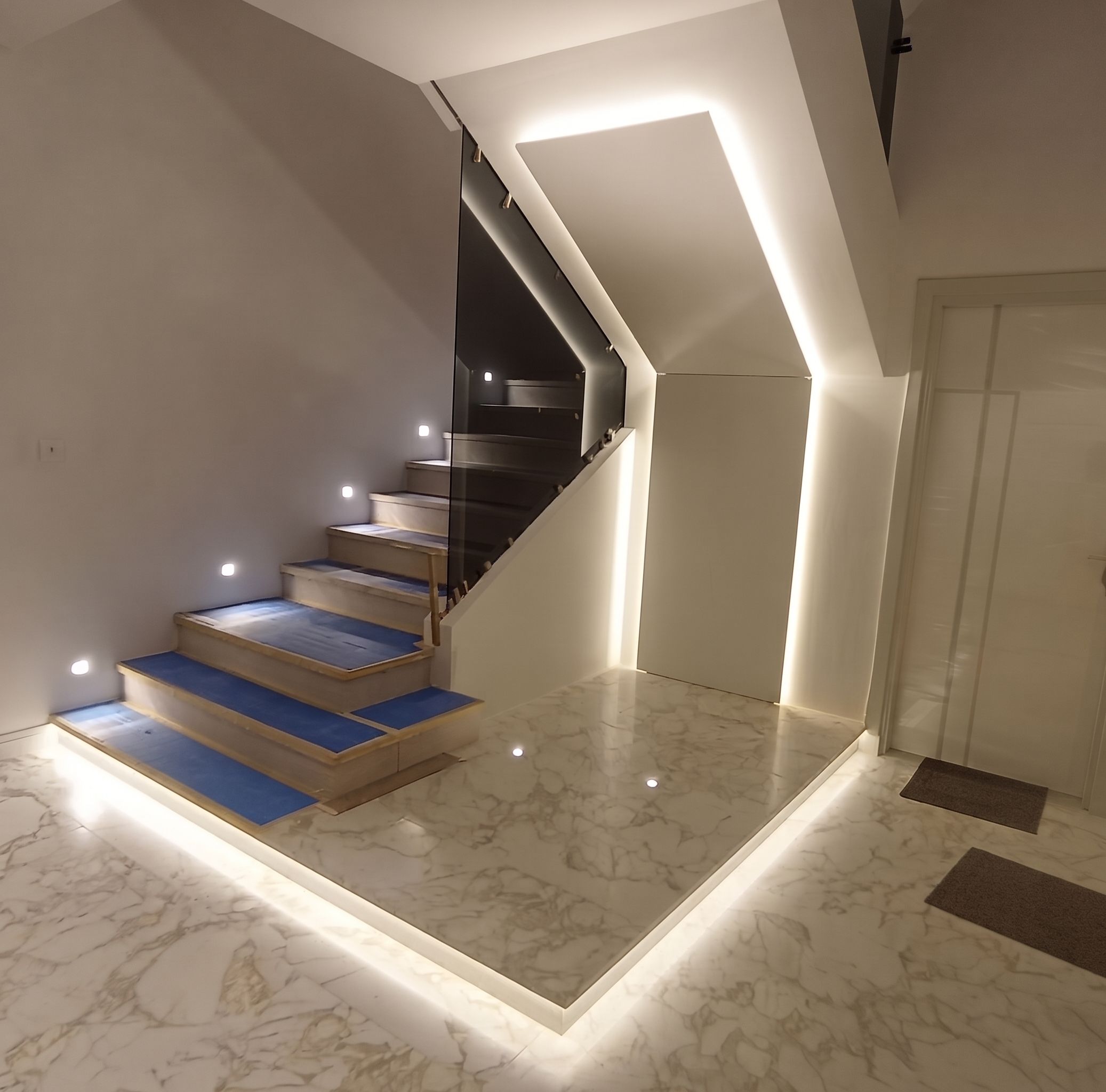 Stone treads with a frameless glass balustrade, step lights in the flanking wall and a lit reveal following the soffit.