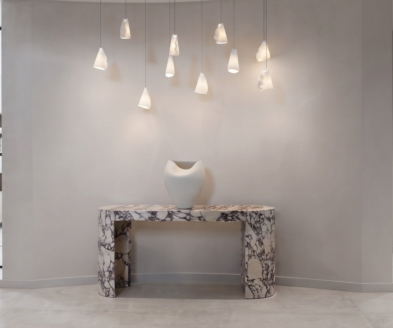 A Viola marble console on a curved micro-cement wall, lit by a scattered cluster of alabaster pendants.