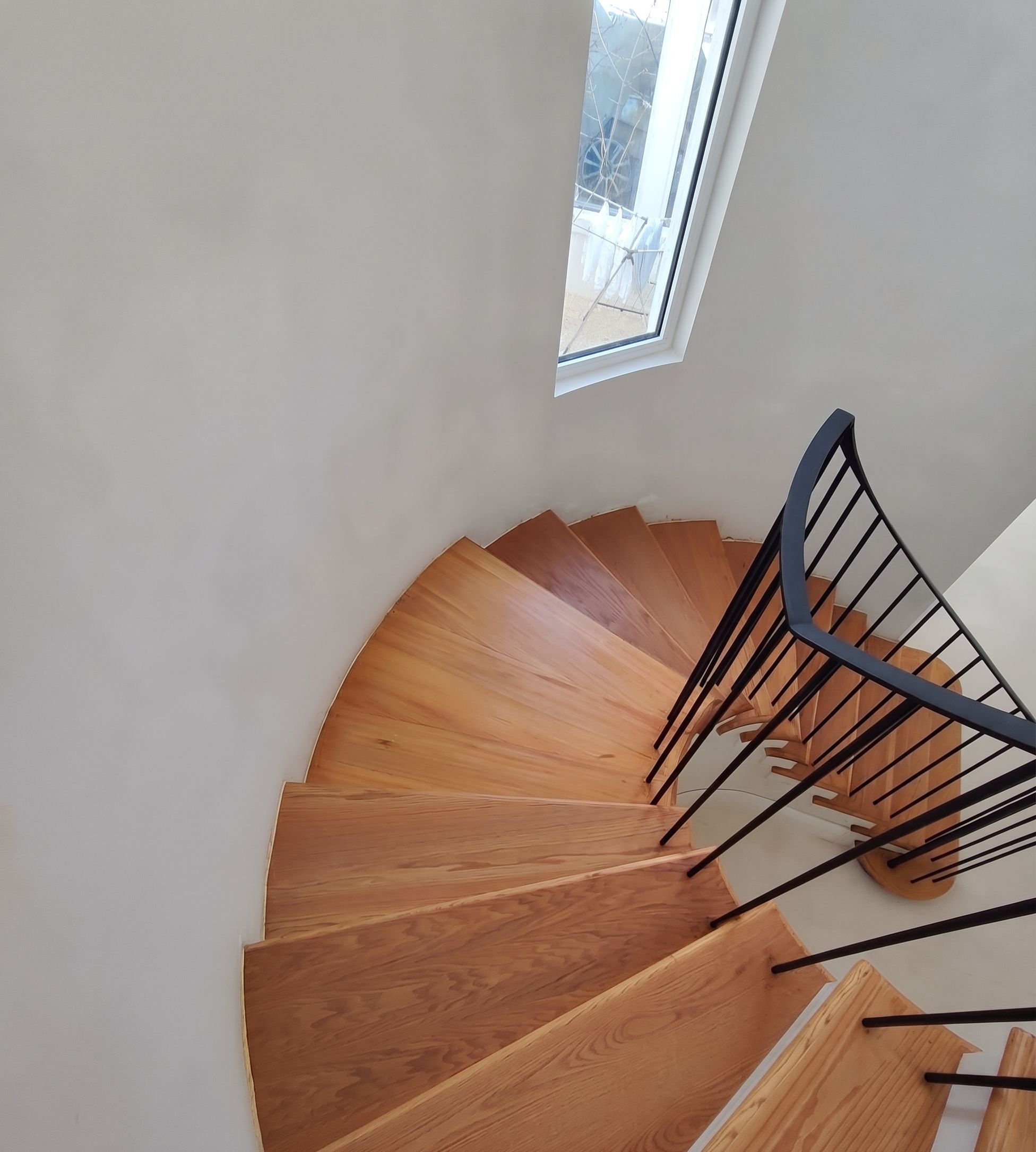 Solid oak treads turning on a curve, with a slim powder-coated steel balustrade and capping rail.