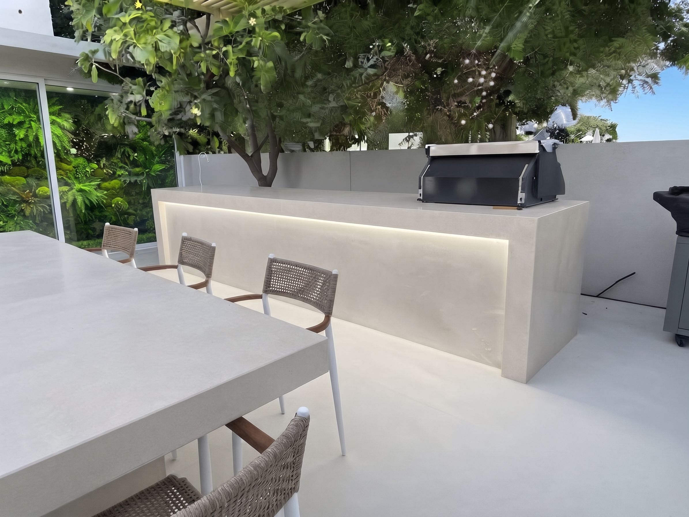 A microcement counter with a lit recess and a built-in grill, facing the dining run under a preserved-moss wall.