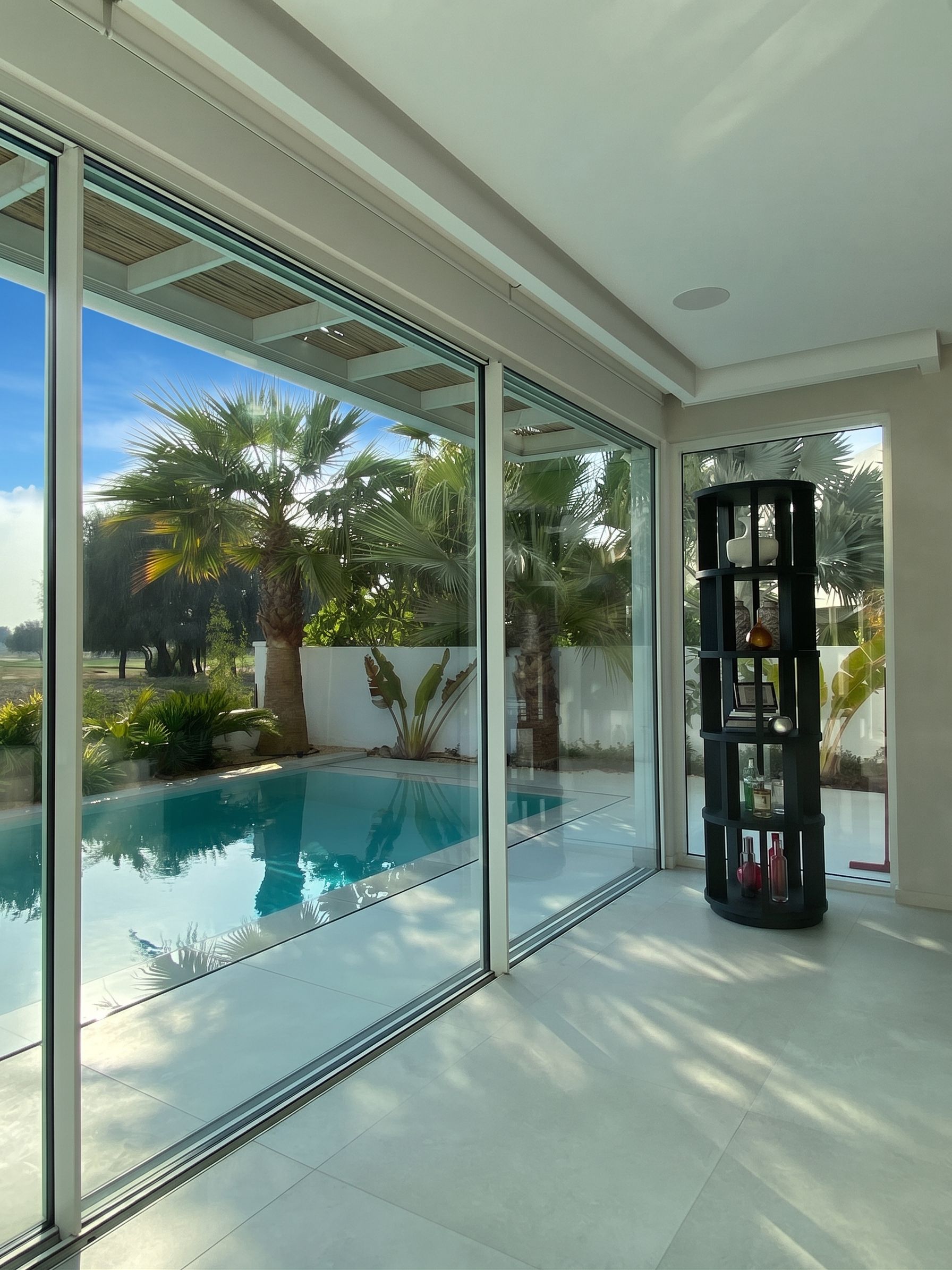 A slim-framed sliding wall opening the living room onto the pool terrace, with a black cylindrical display unit at the return.