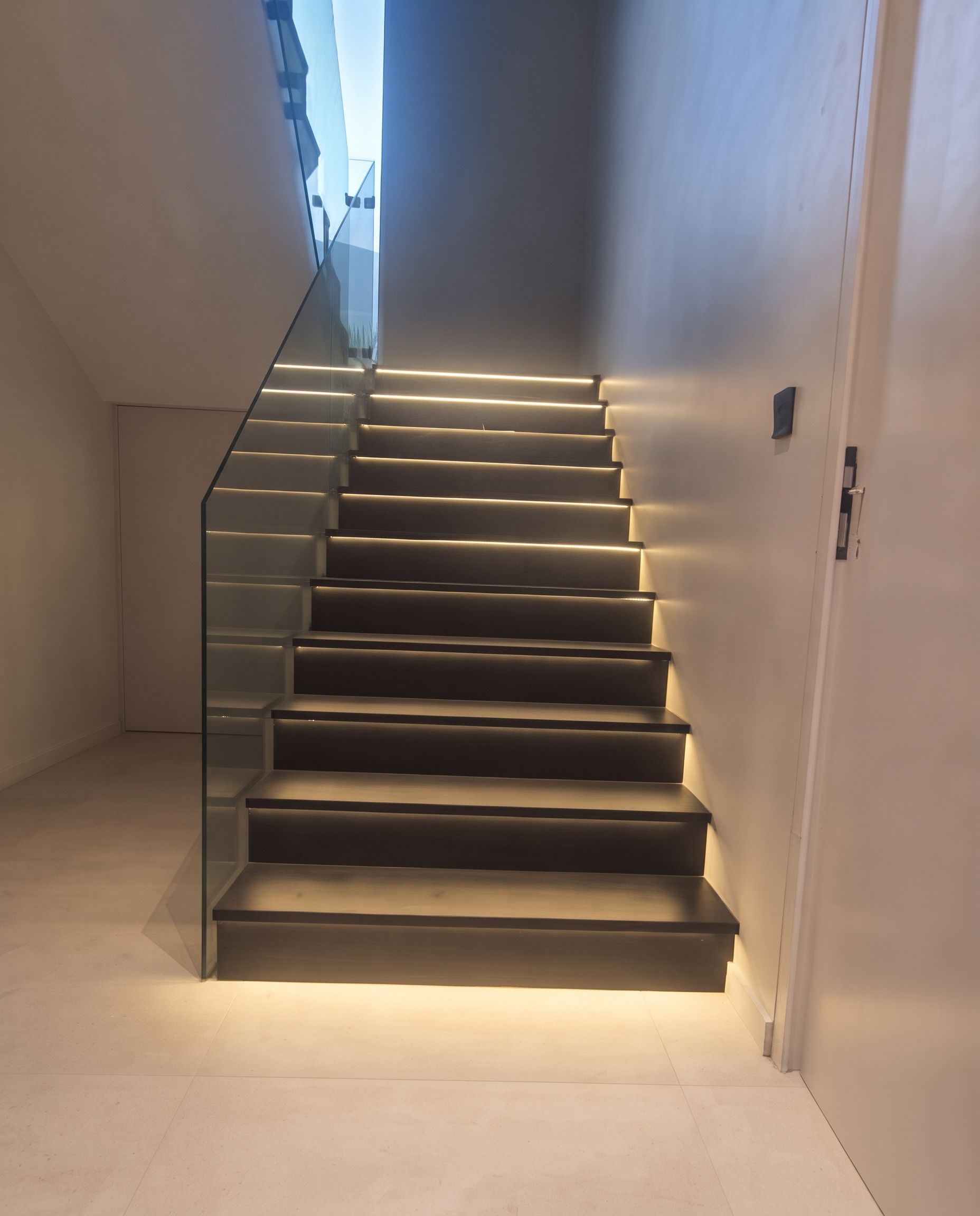 A continuous LED line run under every nosing, with a glass balustrade set into the stringer and no visible fixings.