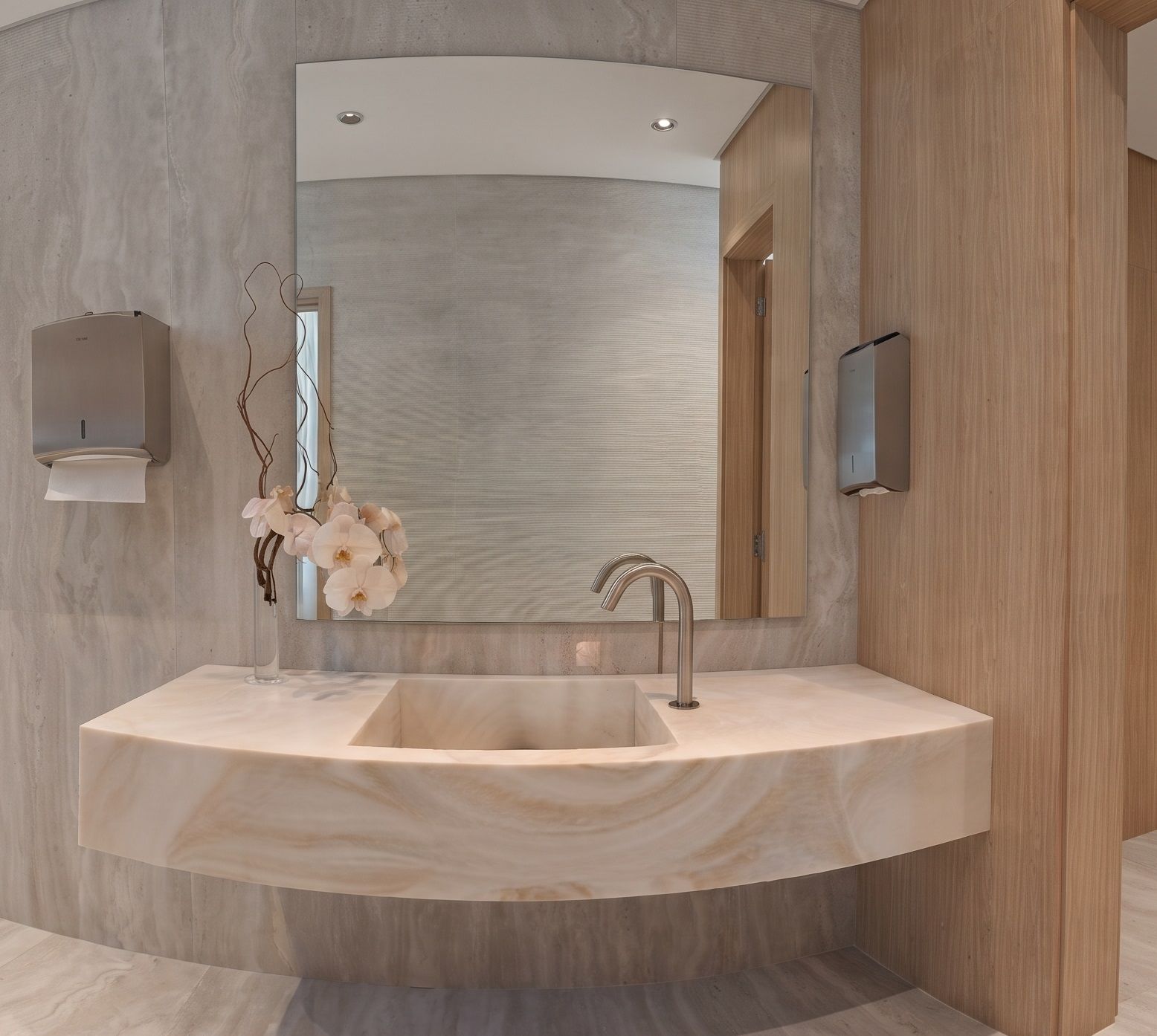 A solid onyx basin carved from one block, set against full-height travertine cladding.