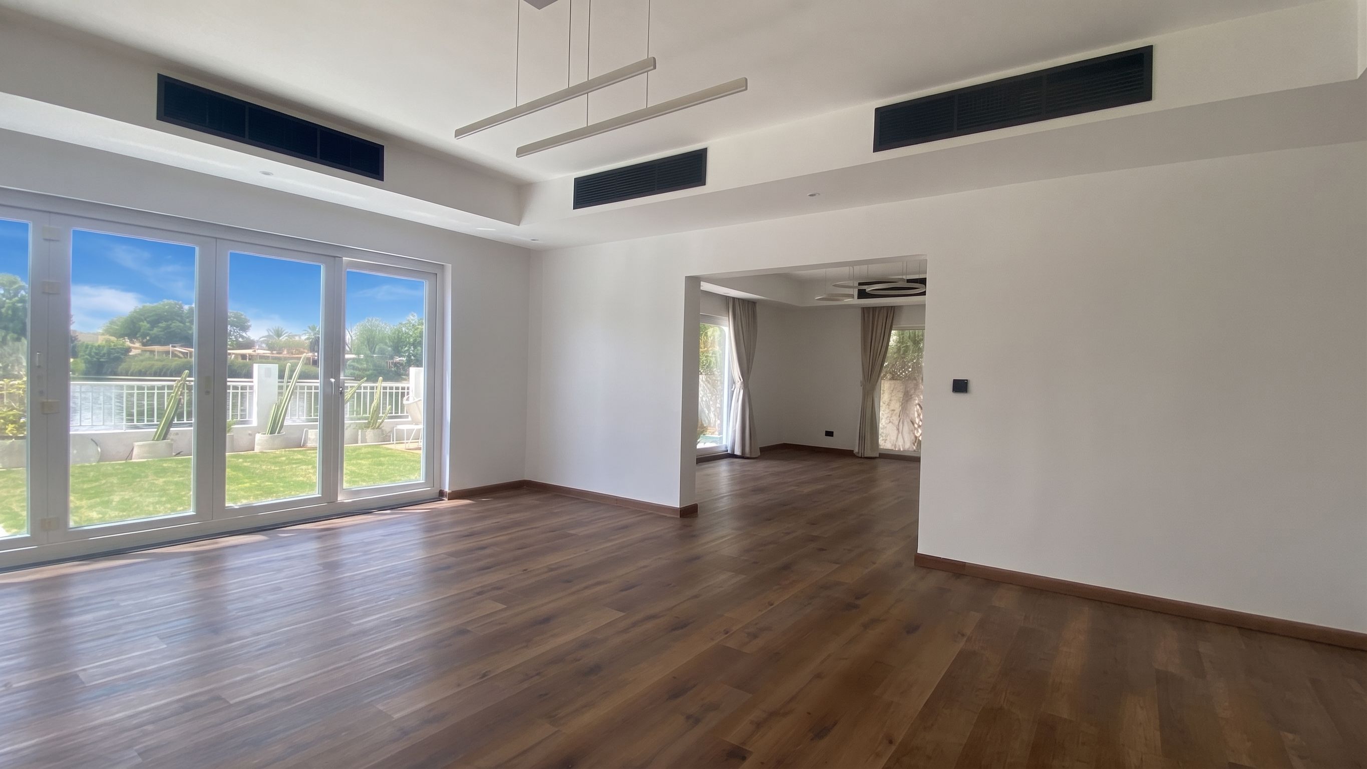 A through room at handover — wide-plank oak flooring, linear pendants over the dining end and slim return grilles set flush into the coffer.