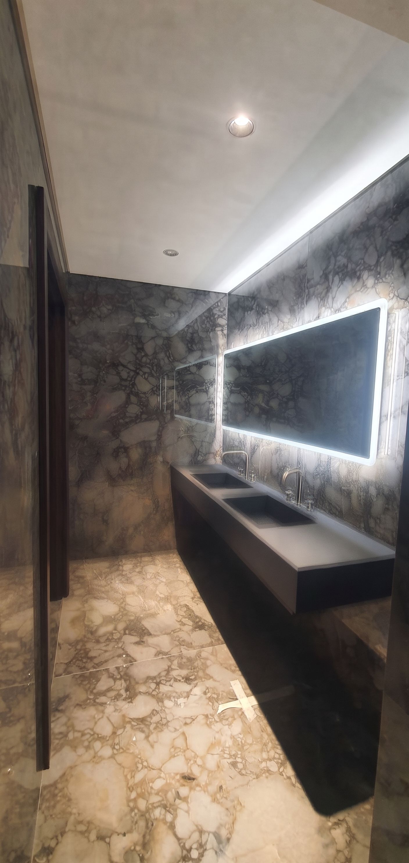 Twin basins cut into a stone counter on a dark floating carcass, against full-height Viola marble and a backlit mirror band.
