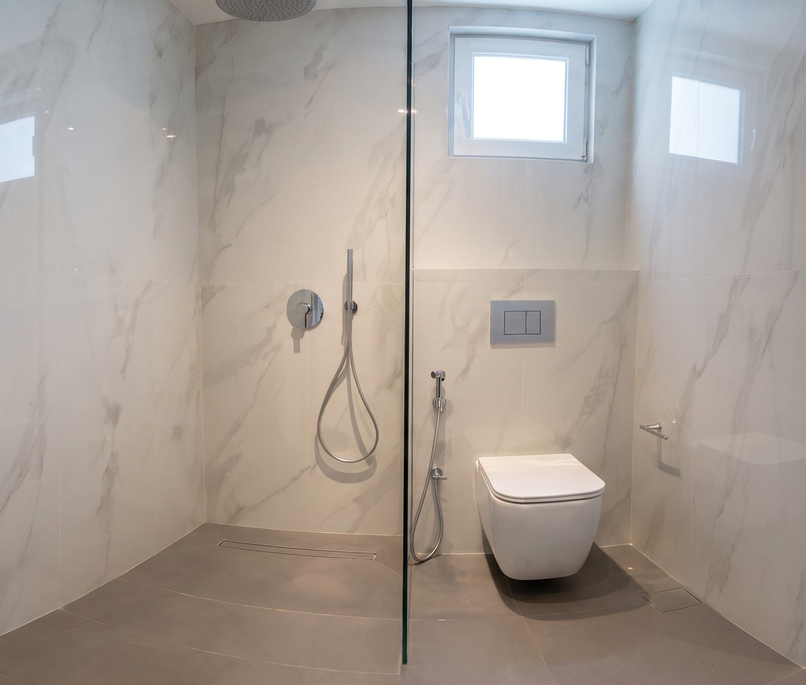A level-access shower on a linear drain, divided from the wall-hung WC by a single pane of glass.